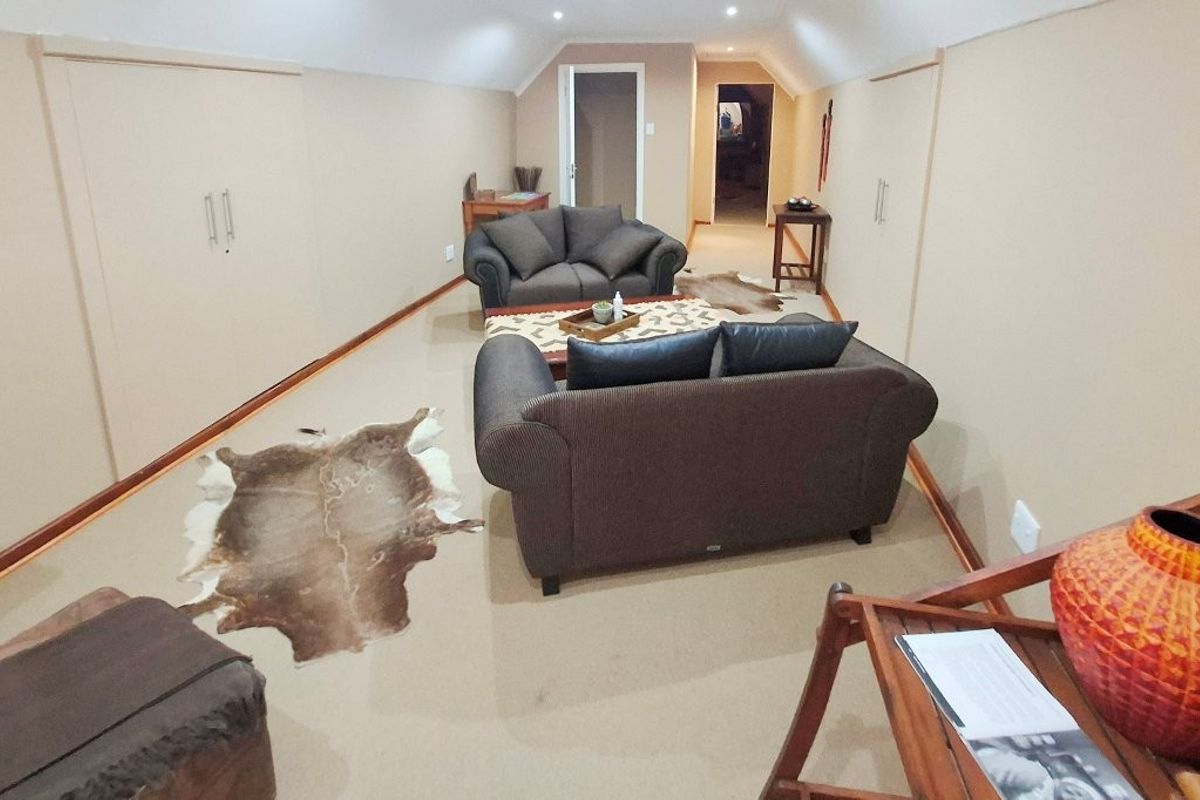 A spacious attic-style living room featuring sloped ceilings, recessed lighting, and built-in storage cupboards along the walls.