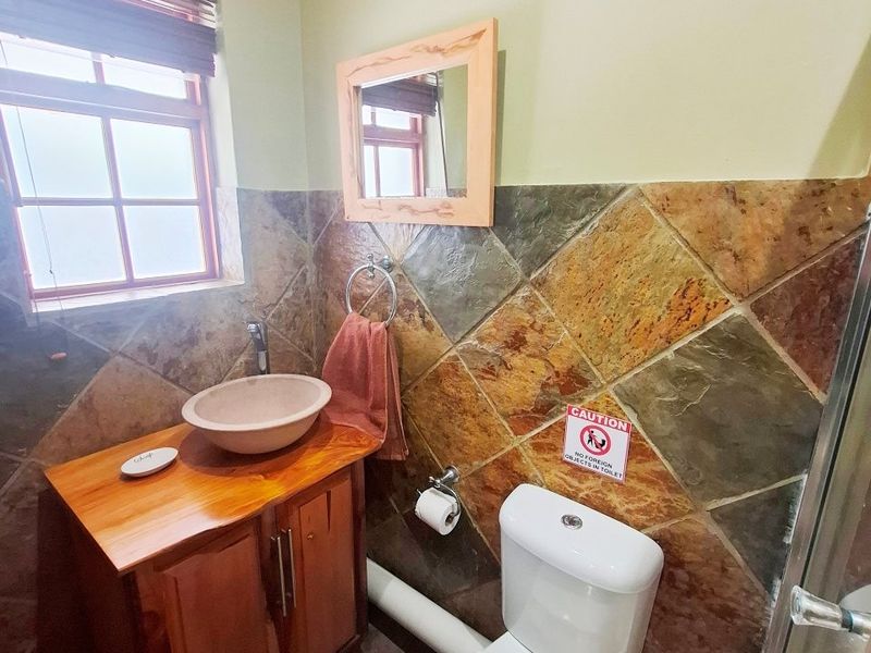 A compact bathroom featuring a wooden vanity with a vessel sink, a standard toilet, and decorative stone-style wall tiling.