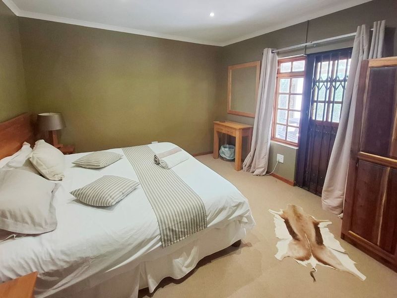 A comfortable bedroom featuring neutral wall tones, carpeted flooring, and a secure wooden door with integrated security gate leading to the exterior.
