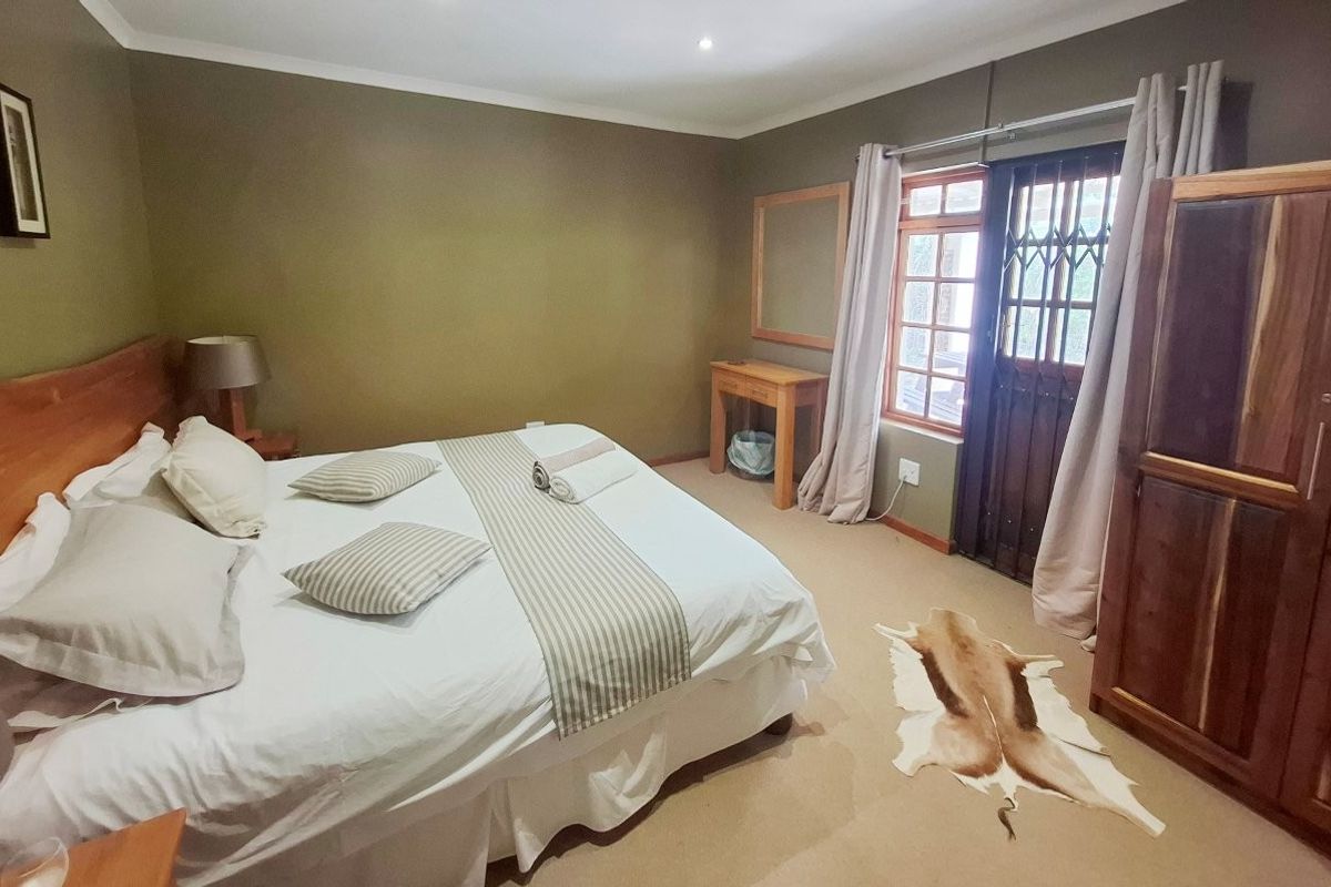 A comfortable bedroom featuring neutral wall tones, carpeted flooring, and a secure wooden door with integrated security gate leading to the exterior.
