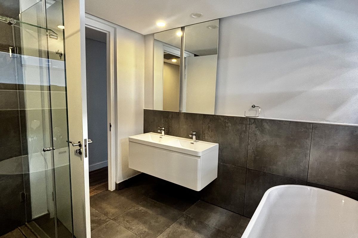 Modern bathroom featuring a floating double vanity, a glass-enclosed walk-in shower, and a freestanding bathtub with large-format dark floor and wall tiles.