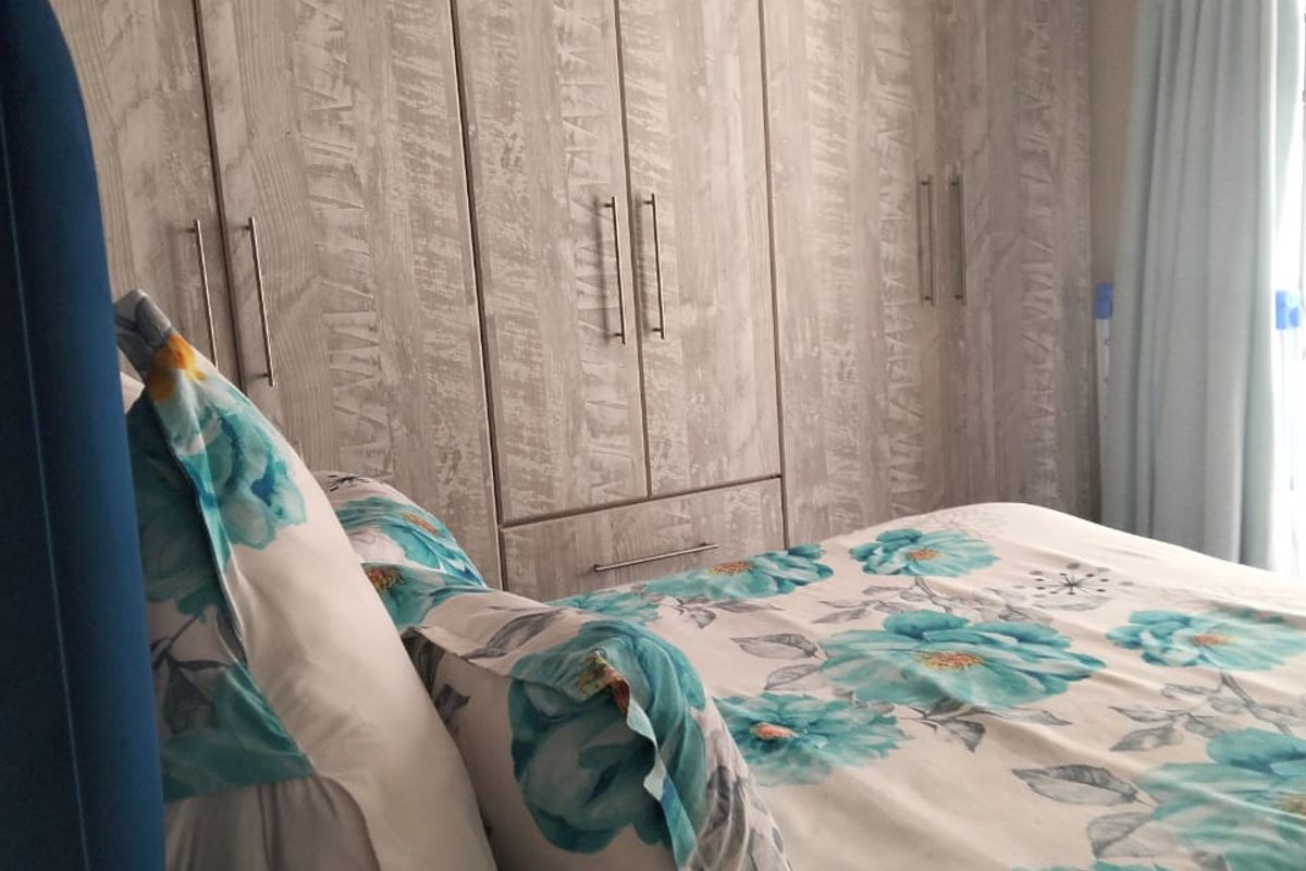 A bedroom featuring floor-to-ceiling built-in wardrobes with a light wood-grain finish and modern metal handles.