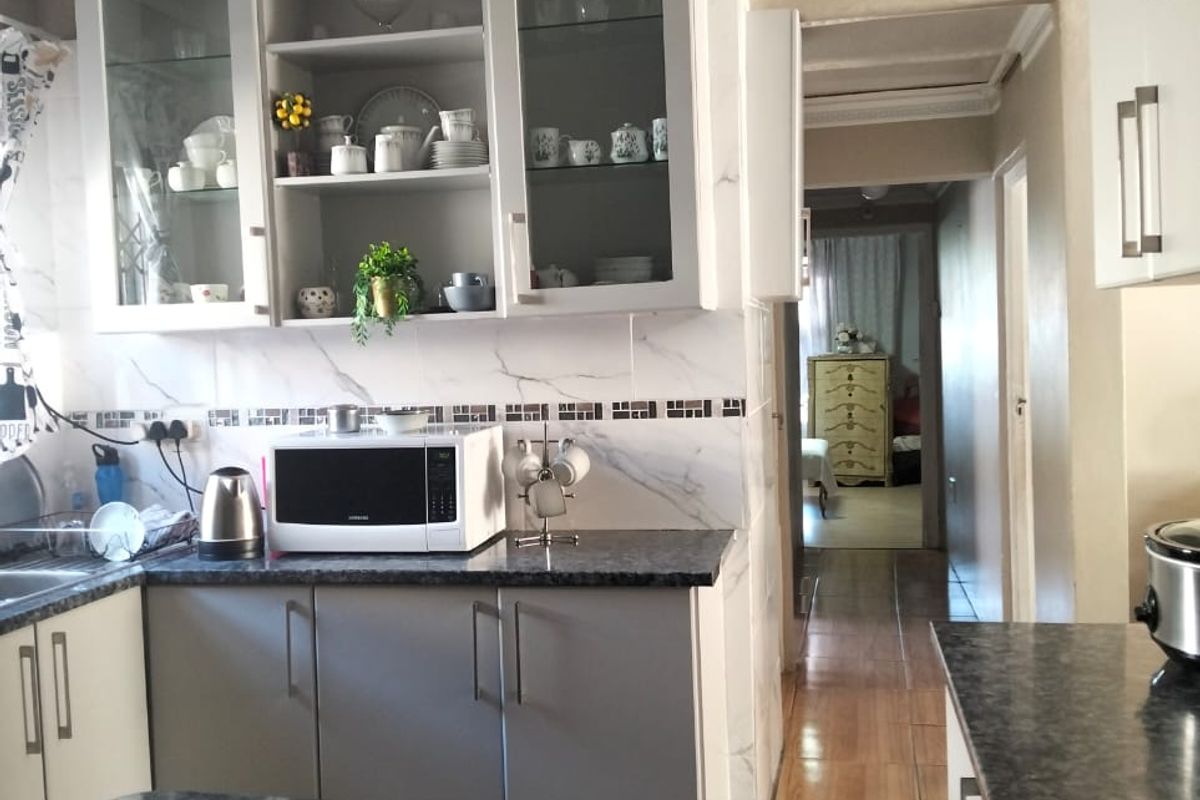 A functional kitchen featuring modern cabinetry, stone-look countertops, marble-effect splashback tiles, and a view through to the hallway and adjacent rooms.