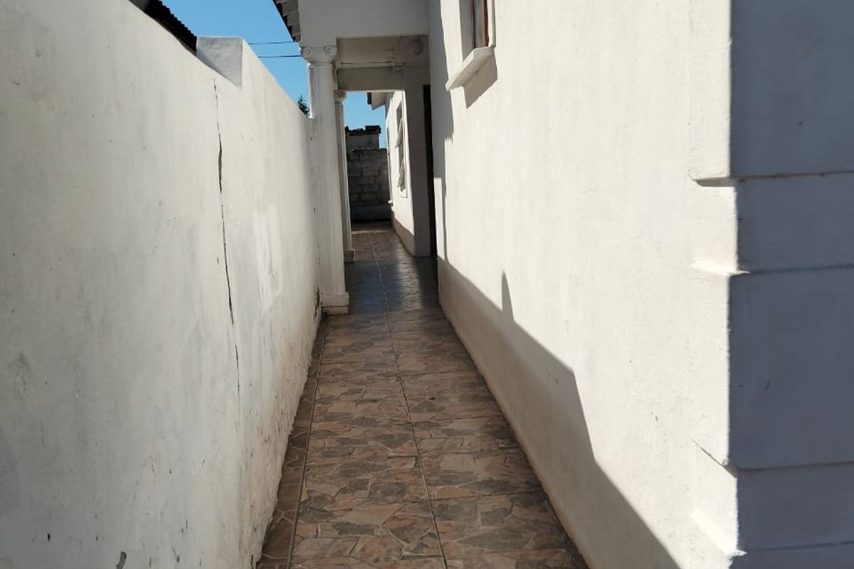 A narrow exterior side walkway featuring tiled flooring and a boundary wall, showing signs of wear and structural cracking.