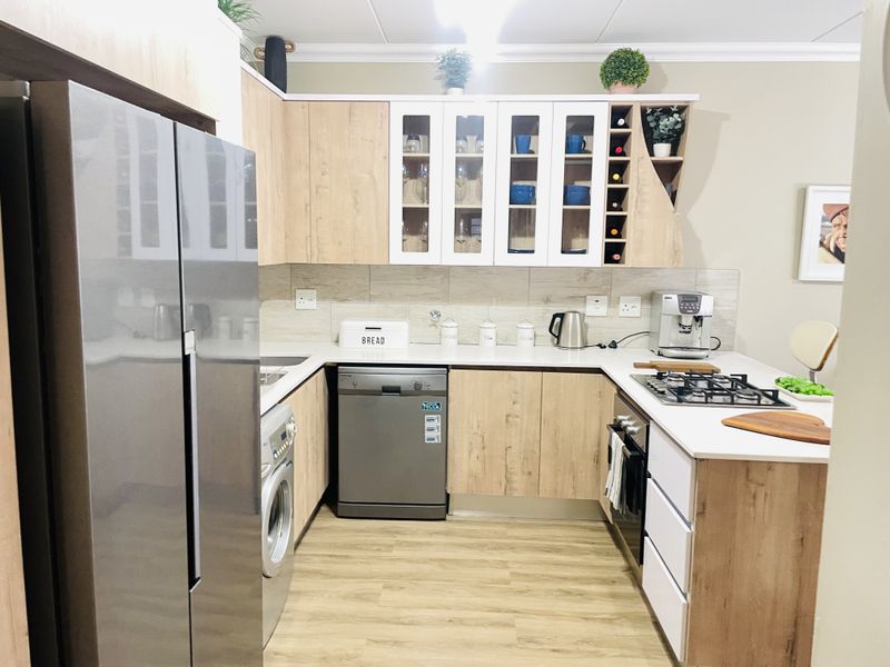 Modern kitchen featuring light wood-tone cabinetry, white countertops, a gas hob, built-in oven, and integrated storage with a dedicated wine rack.