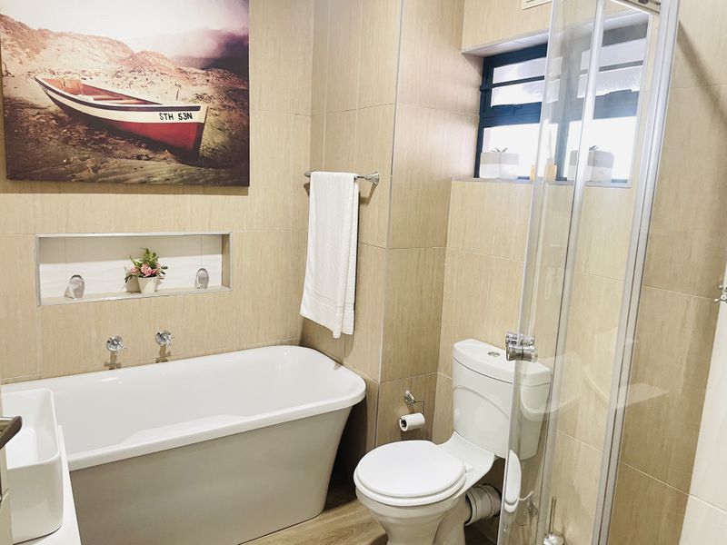Modern bathroom featuring a freestanding bathtub, glass-enclosed shower, recessed wall niche, and neutral floor-to-ceiling tiling.