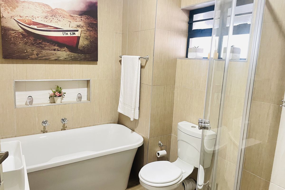 Modern bathroom featuring a freestanding bathtub, glass-enclosed shower, recessed wall niche, and neutral floor-to-ceiling tiling.