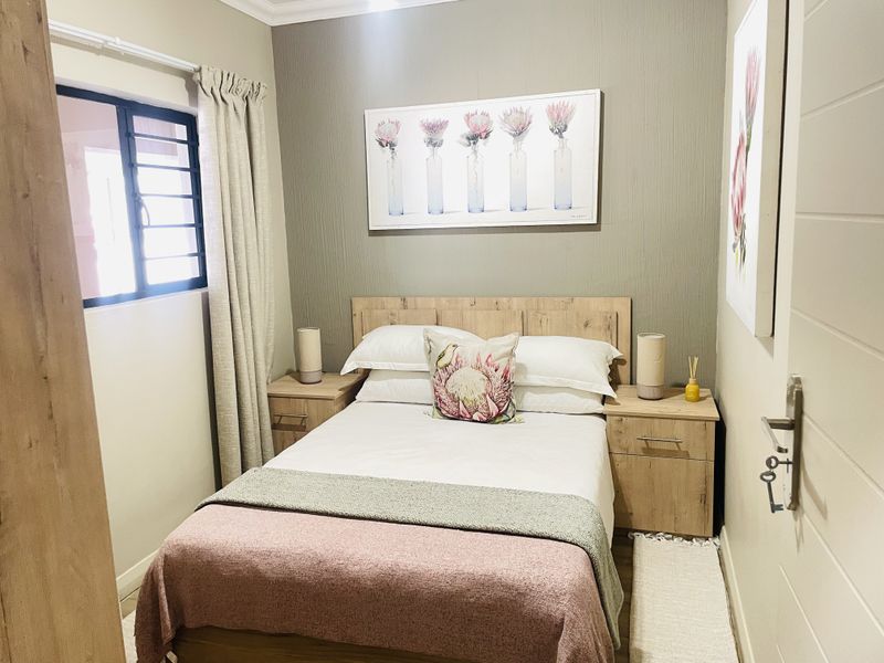 A cozy bedroom featuring a textured accent wall, neutral tones, and a window fitted with security burglar bars.