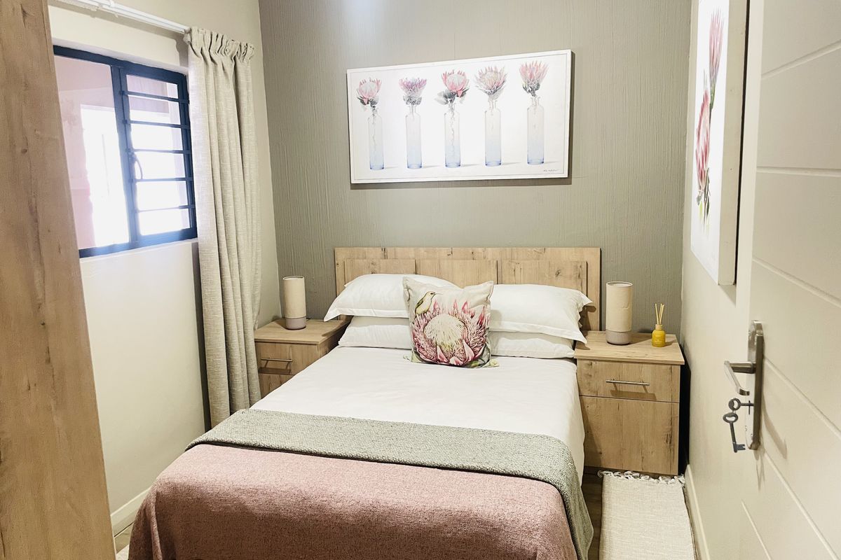 A cozy bedroom featuring a textured accent wall, neutral tones, and a window fitted with security burglar bars.