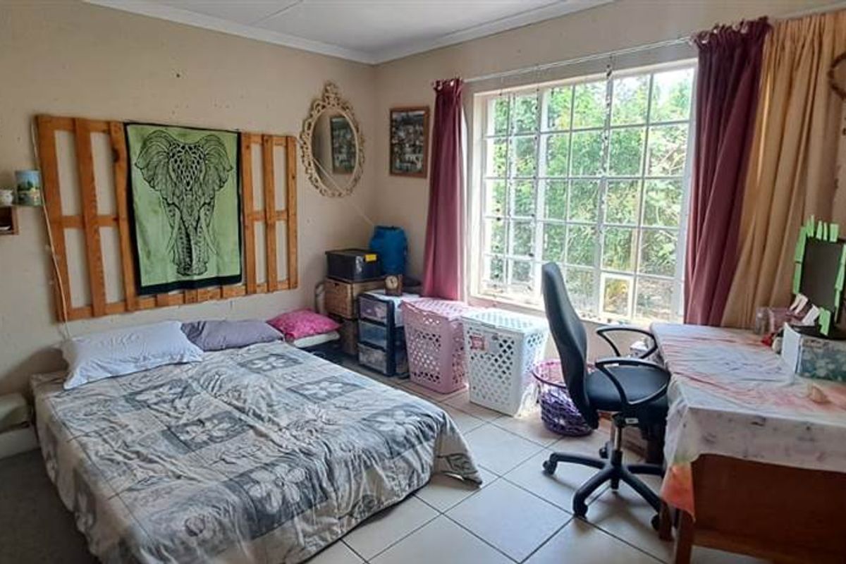 A bedroom featuring tiled flooring and a large window, providing natural light and a functional layout for a sleeping and study area.