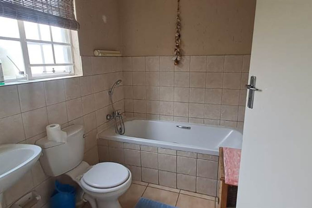 A functional bathroom featuring a built-in bathtub with shower attachment, pedestal basin, and toilet, finished with neutral wall and floor tiling.