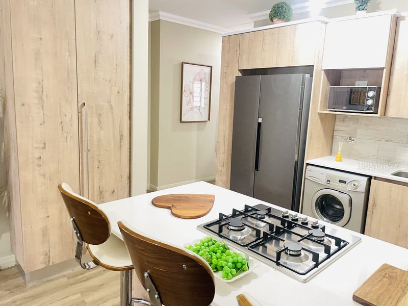 Modern kitchen featuring light wood-grain cabinetry, stone countertops, a built-in gas hob, and integrated appliances including a washing machine and microwave.