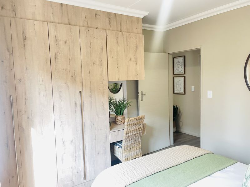 A well-maintained bedroom featuring modern wood-finish built-in cupboards with an integrated vanity area and neutral wall tones.