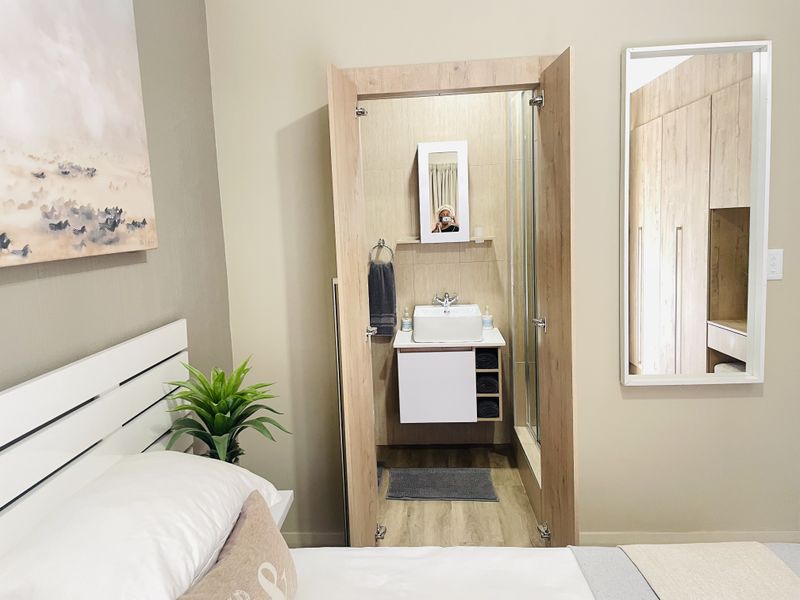 A modern bedroom featuring an integrated en-suite bathroom with a vessel sink vanity and shower, complemented by built-in wooden cabinetry.