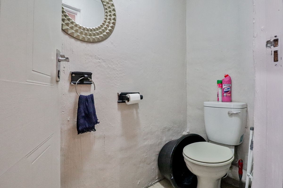 A compact bathroom featuring a standard toilet, wall-mounted mirror, and towel ring, currently requiring cosmetic updates to the wall finishes and door frame.