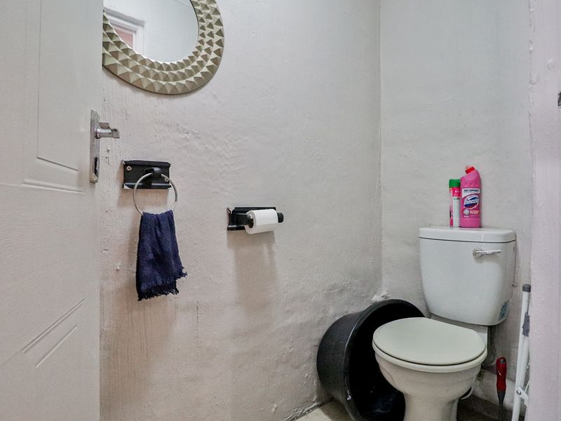 A compact bathroom featuring a standard toilet, wall-mounted mirror, and towel ring, currently requiring cosmetic updates to the wall finishes and door frame.