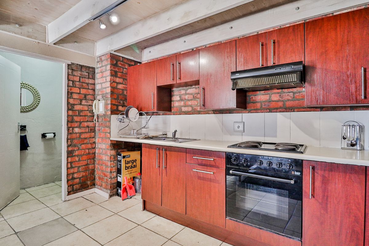 Kitchen featuring dark wood cabinetry, exposed brick walls, tiled flooring, and built-in oven and hob, with an adjacent doorway leading to a bathroom.