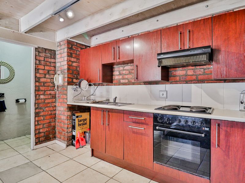 Kitchen featuring dark wood cabinetry, exposed brick walls, tiled flooring, and built-in oven and hob, with an adjacent doorway leading to a bathroom.