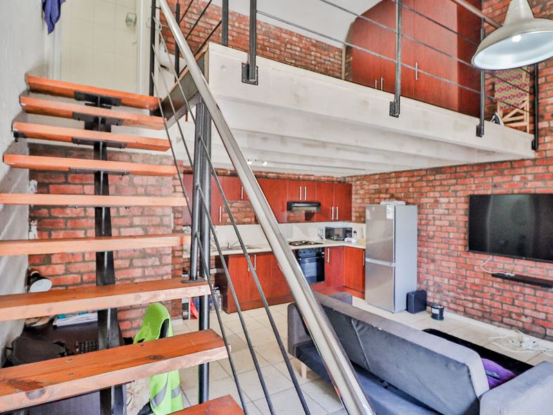 Open-plan living area featuring exposed brick walls, a mezzanine level, and a functional kitchen with built-in cabinetry and appliances.