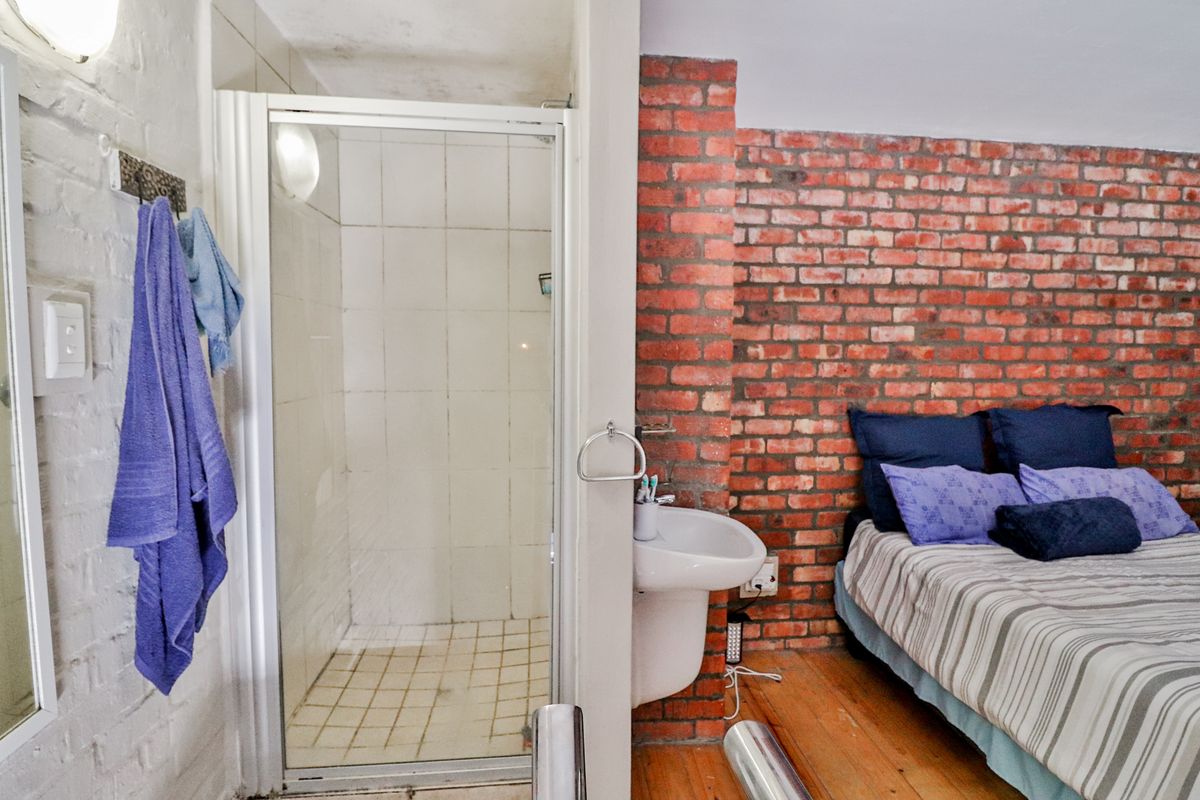 Bedroom featuring an open-plan layout with an integrated shower cubicle, wall-mounted basin, and exposed brick feature wall.