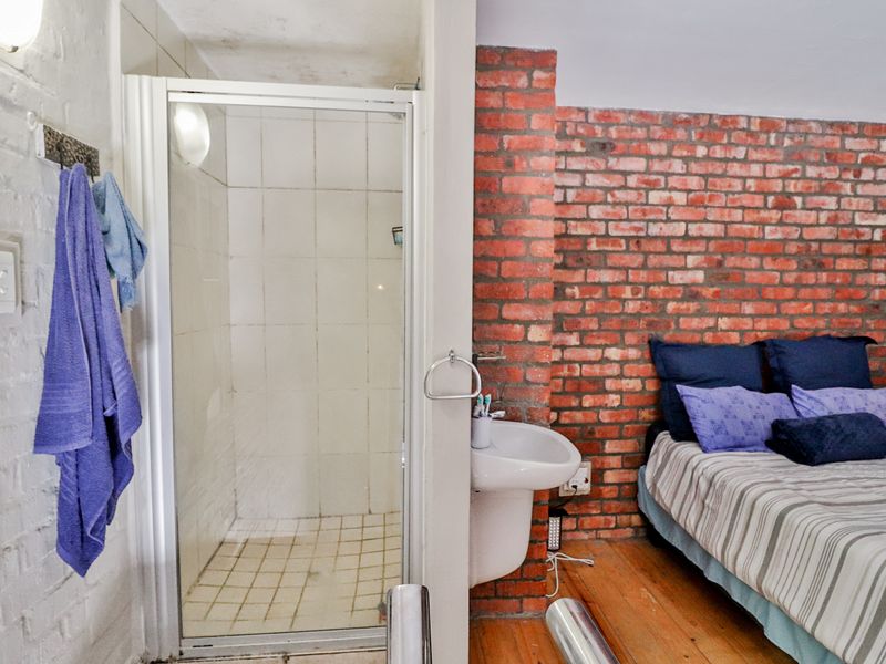 Bedroom featuring an open-plan layout with an integrated shower cubicle, wall-mounted basin, and exposed brick feature wall.