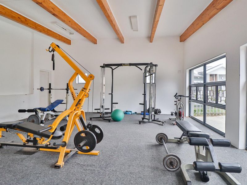 A spacious home gym featuring exposed timber ceiling beams, large windows providing natural light, and durable carpet flooring.