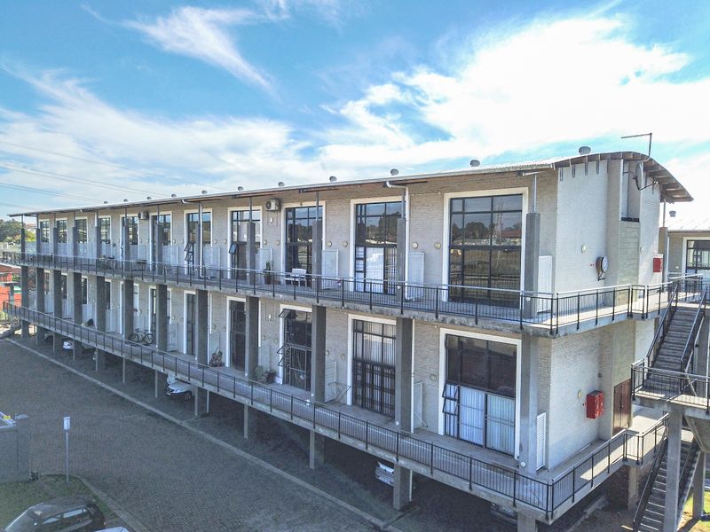 An aerial view of a multi-story apartment building featuring industrial-style brick architecture, large windows, and external balcony walkways.