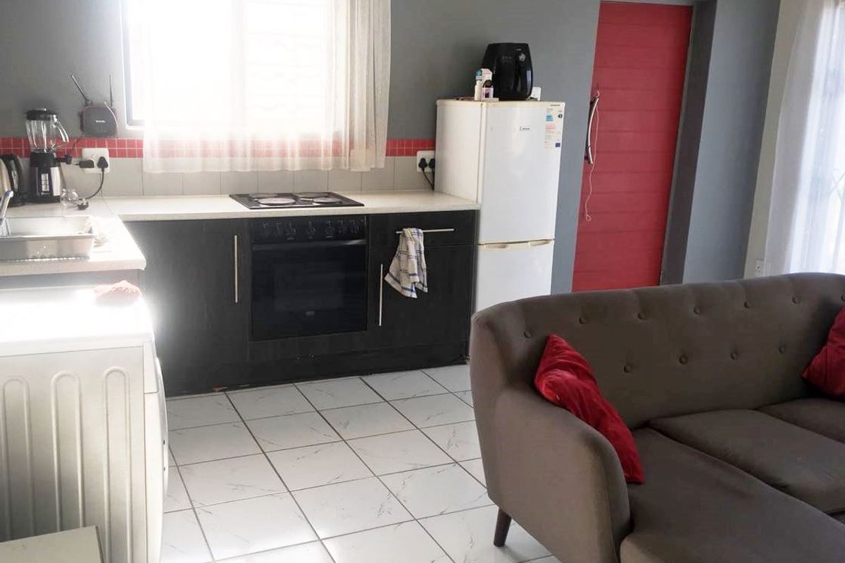 Open plan living area featuring a compact kitchen with built-in oven, electric hob, tiled backsplash, and light-colored tiled flooring throughout.