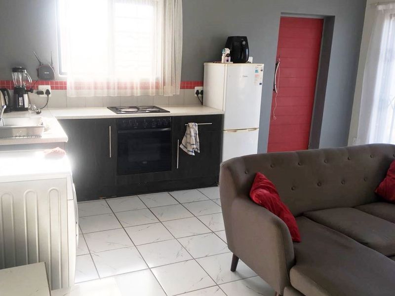 Open plan living area featuring a compact kitchen with built-in oven, electric hob, tiled backsplash, and light-colored tiled flooring throughout.