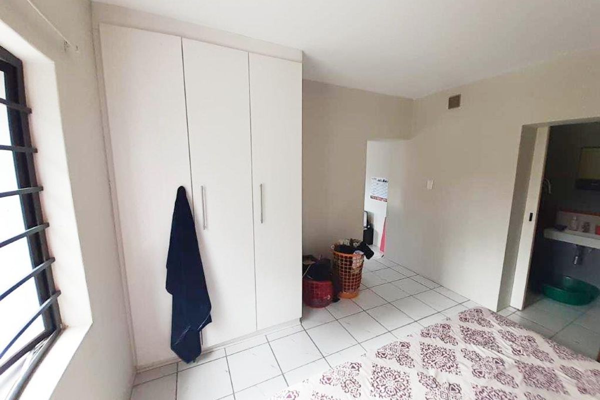 A bedroom featuring tiled flooring, a built-in wardrobe, and a window with security bars, with an adjacent view into a bathroom area.
