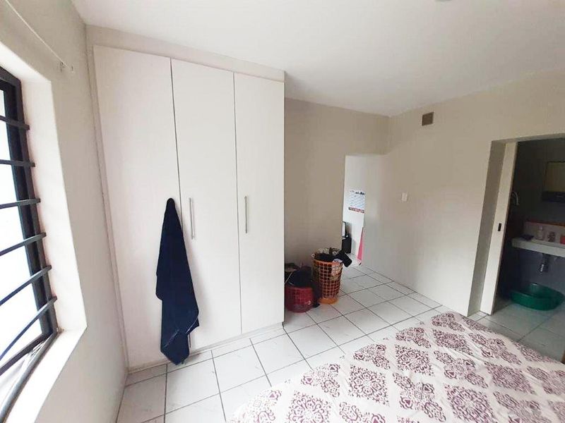 A bedroom featuring tiled flooring, a built-in wardrobe, and a window with security bars, with an adjacent view into a bathroom area.