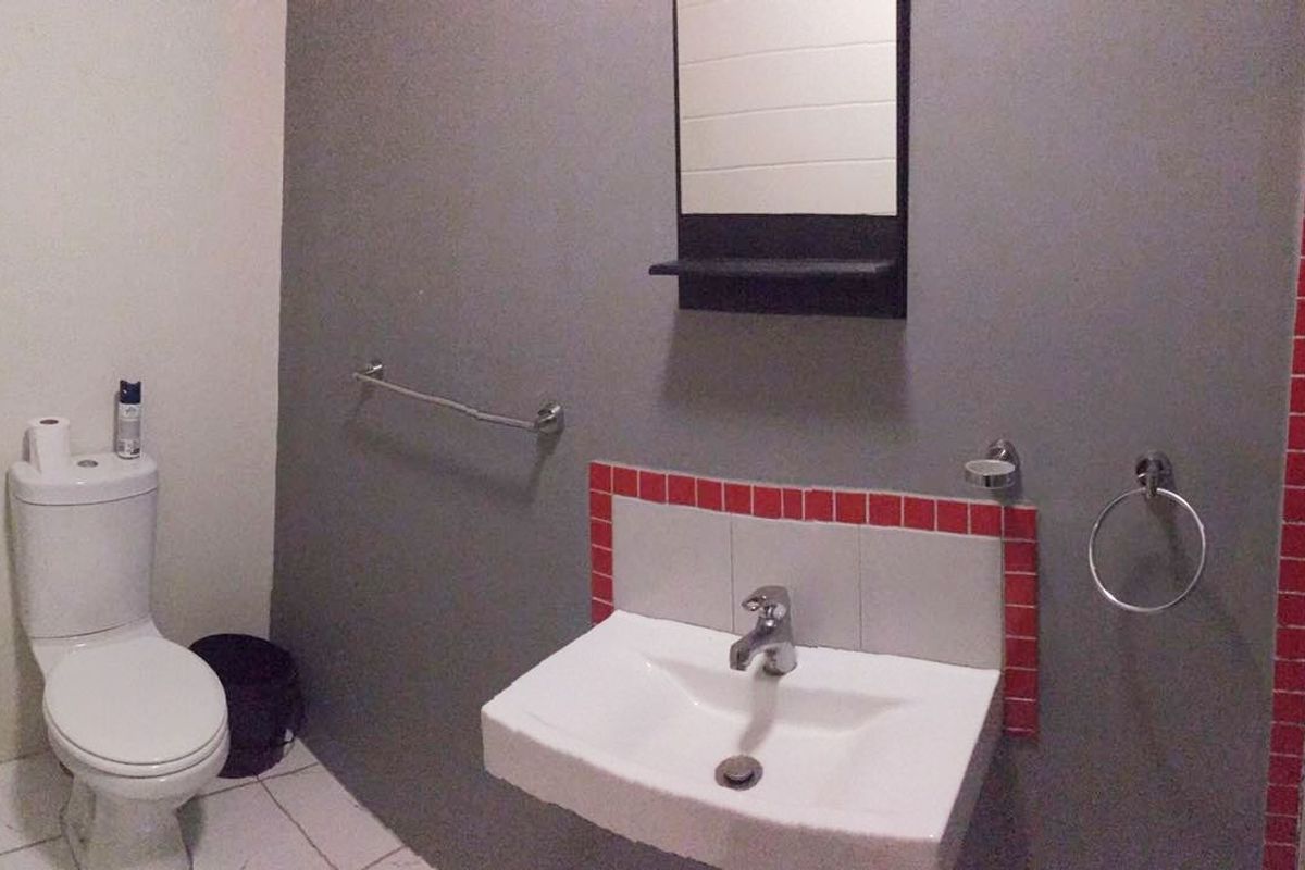 A functional bathroom featuring a wall-mounted basin with a tiled splashback, a toilet, and essential bathroom fixtures.