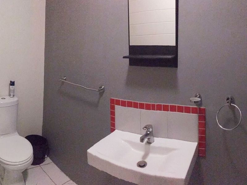 A functional bathroom featuring a wall-mounted basin with a tiled splashback, a toilet, and essential bathroom fixtures.