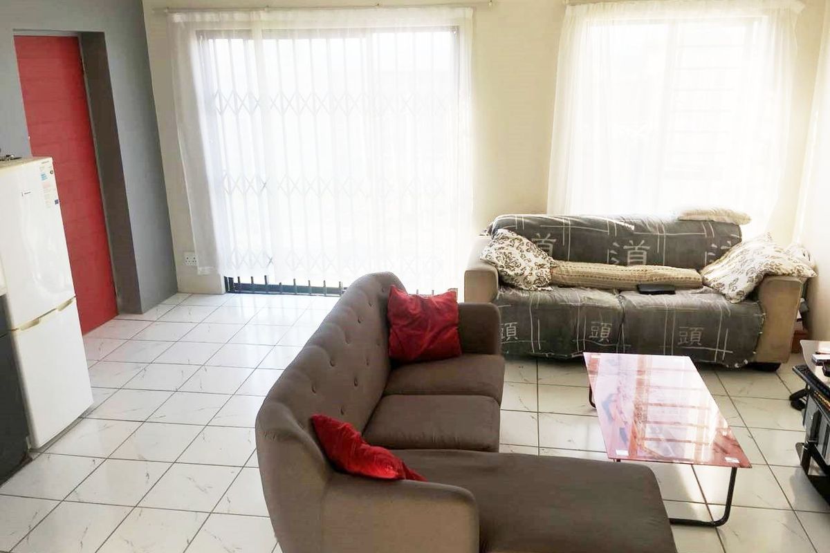 A living room area featuring tiled flooring and a sliding glass door with a security gate, providing access to the exterior.