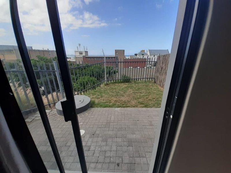 A private outdoor patio area featuring paved flooring, a small grass lawn, and metal perimeter fencing, accessible via a sliding glass door.