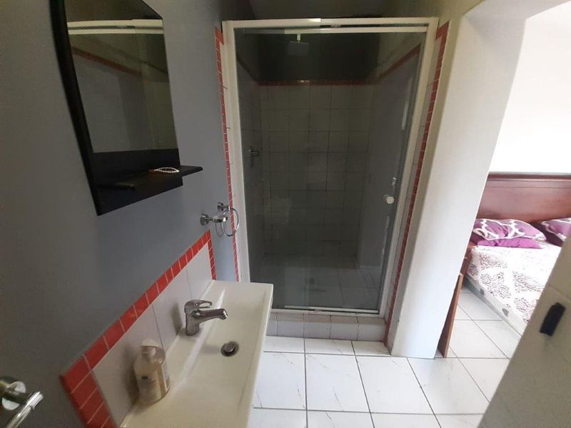 A functional bathroom featuring a shower enclosure, wall-mounted basin, and tiled finishes, conveniently located adjacent to the bedroom area.