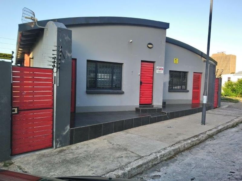 Front exterior view of a property featuring a grey facade, red security gates, tiled porch area, and perimeter electric fencing.