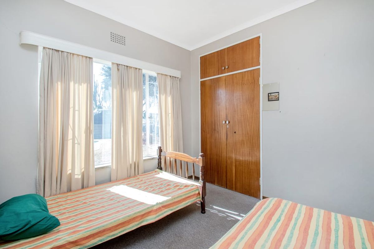 A bedroom featuring built-in wooden cupboards, carpeted flooring, and large windows allowing for natural light.
