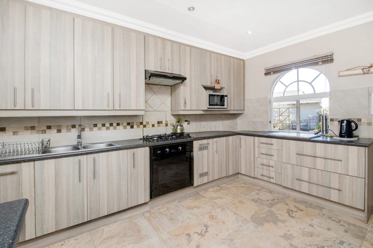 A well-maintained kitchen featuring light wood-grain cabinetry, dark countertops, a built-in gas hob, oven, extractor fan, and a distinctive arched window.