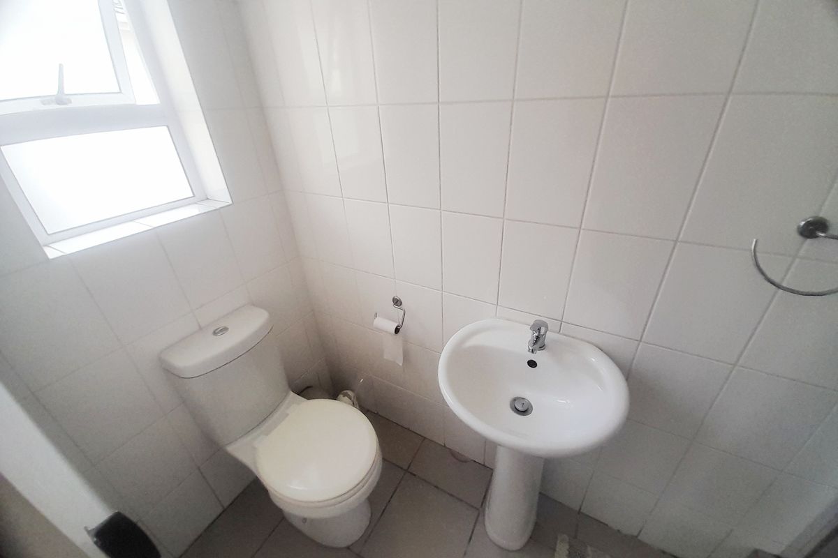 A compact bathroom featuring a pedestal basin, toilet, and neutral wall tiling, providing a functional and clean space.