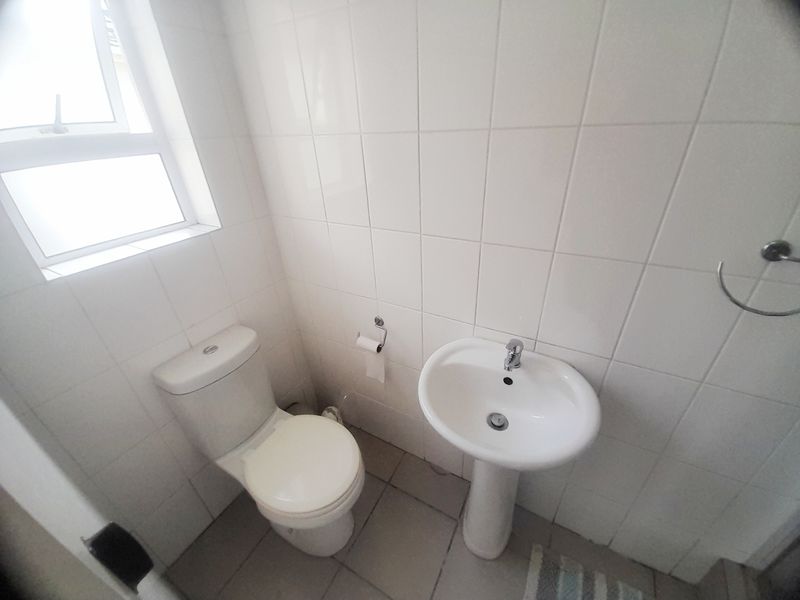 A compact bathroom featuring a pedestal basin, toilet, and neutral wall tiling, providing a functional and clean space.