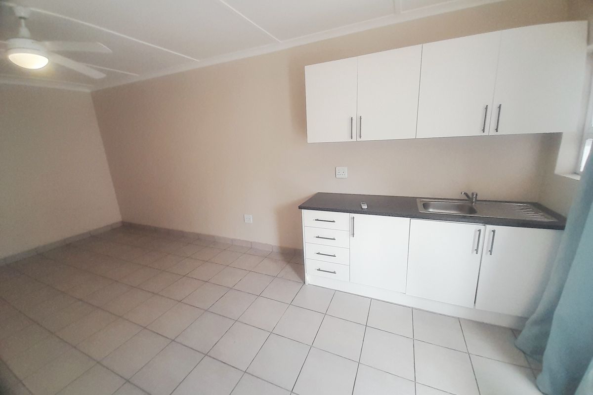 A compact, empty kitchen area featuring white cabinetry, a dark laminate countertop, stainless steel sink, and tiled flooring.