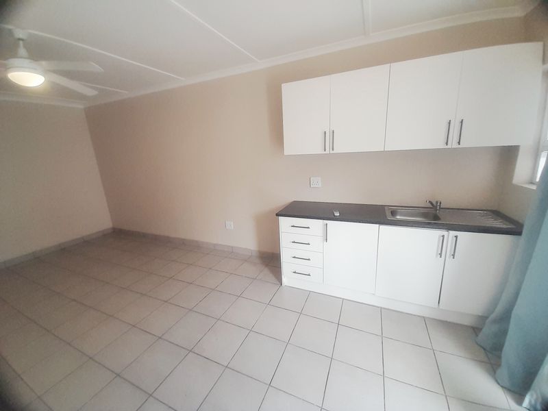 A compact, empty kitchen area featuring white cabinetry, a dark laminate countertop, stainless steel sink, and tiled flooring.