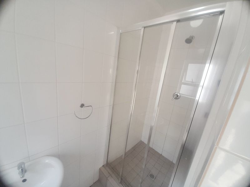 A functional bathroom featuring a glass-enclosed shower with tiled walls and a wall-mounted washbasin.