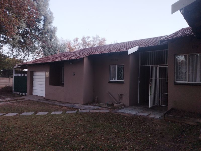 Front elevation of a single-story house featuring a tiled roof, integrated garage, and security gate entrance with a paved walkway.