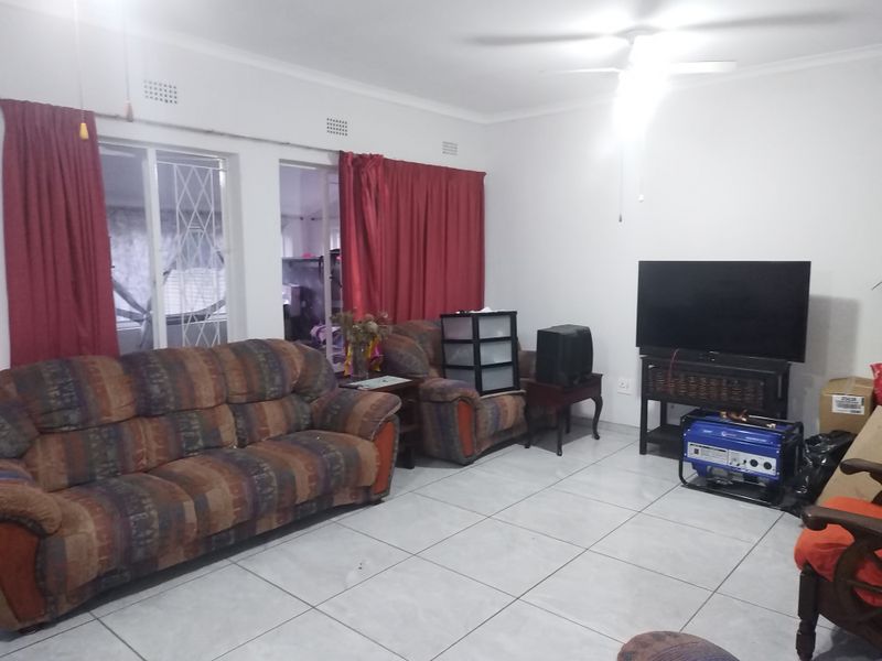 A living room featuring ceramic floor tiles, a ceiling fan, and a sliding door with security gate access.