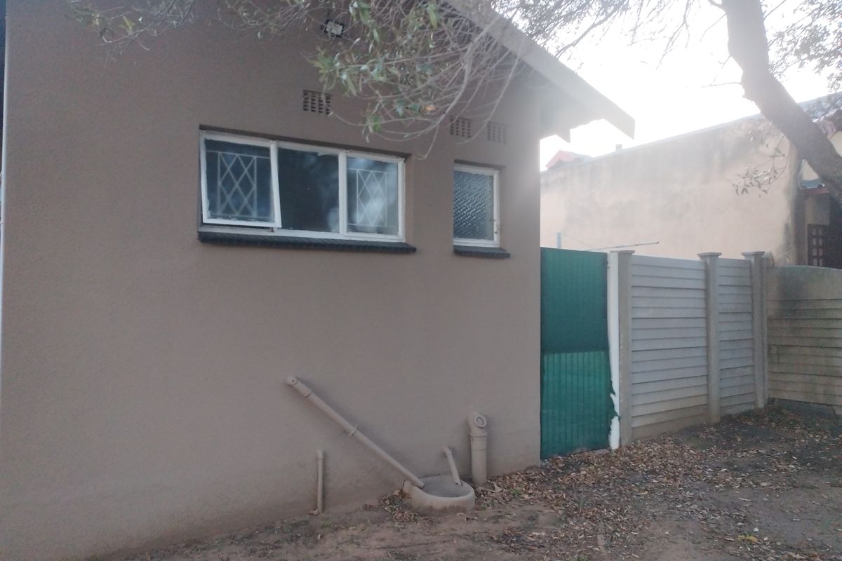 Rear exterior view of the property featuring a precast concrete boundary wall, security-barred windows, and external drainage infrastructure.