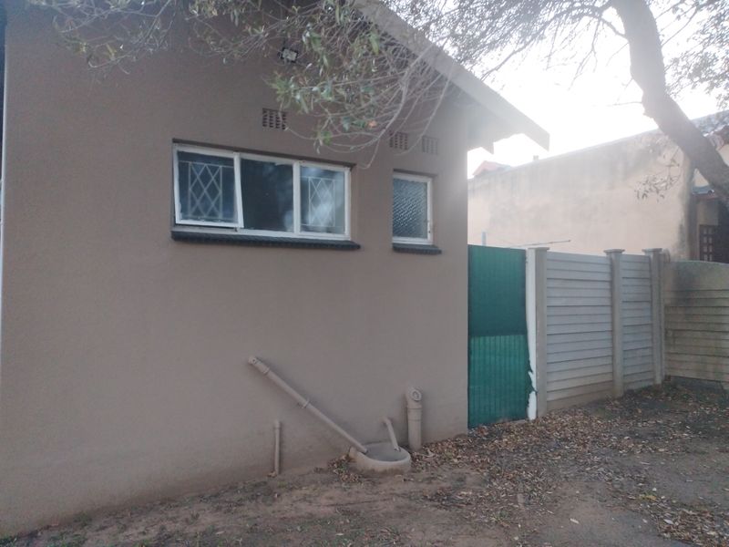 Rear exterior view of the property featuring a precast concrete boundary wall, security-barred windows, and external drainage infrastructure.