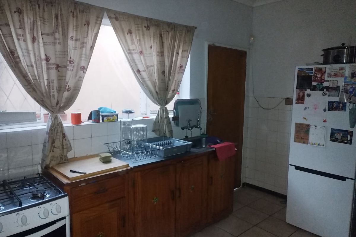 A functional kitchen featuring wooden cabinetry, a gas stove, and tiled splashbacks, offering a practical layout with potential for modern cosmetic updates.