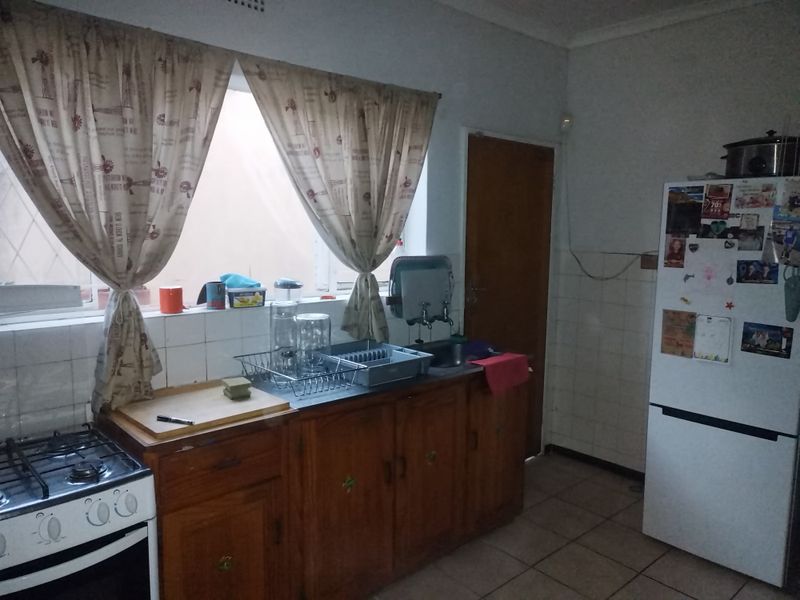 A functional kitchen featuring wooden cabinetry, a gas stove, and tiled splashbacks, offering a practical layout with potential for modern cosmetic updates.